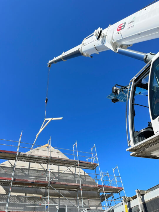 Ein Mobilkran der GB hebt ein Dachelement in den Rohbau