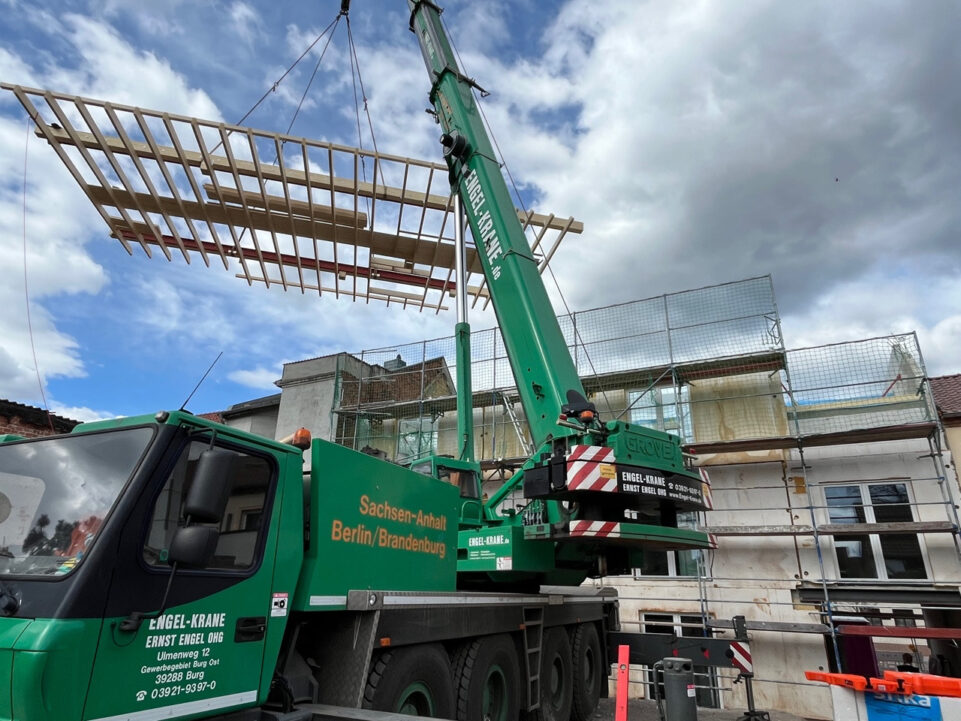 Dachstuhlteile werden mit einem mobilen Kran an ihre Position gehoben